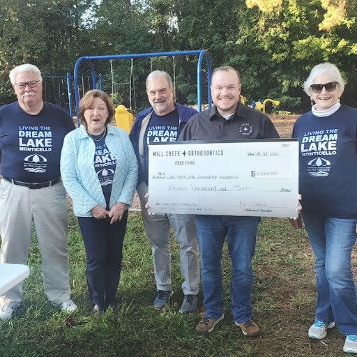 5 People standing in a playground holding a large check to donated from Mill Creek Orthodontics